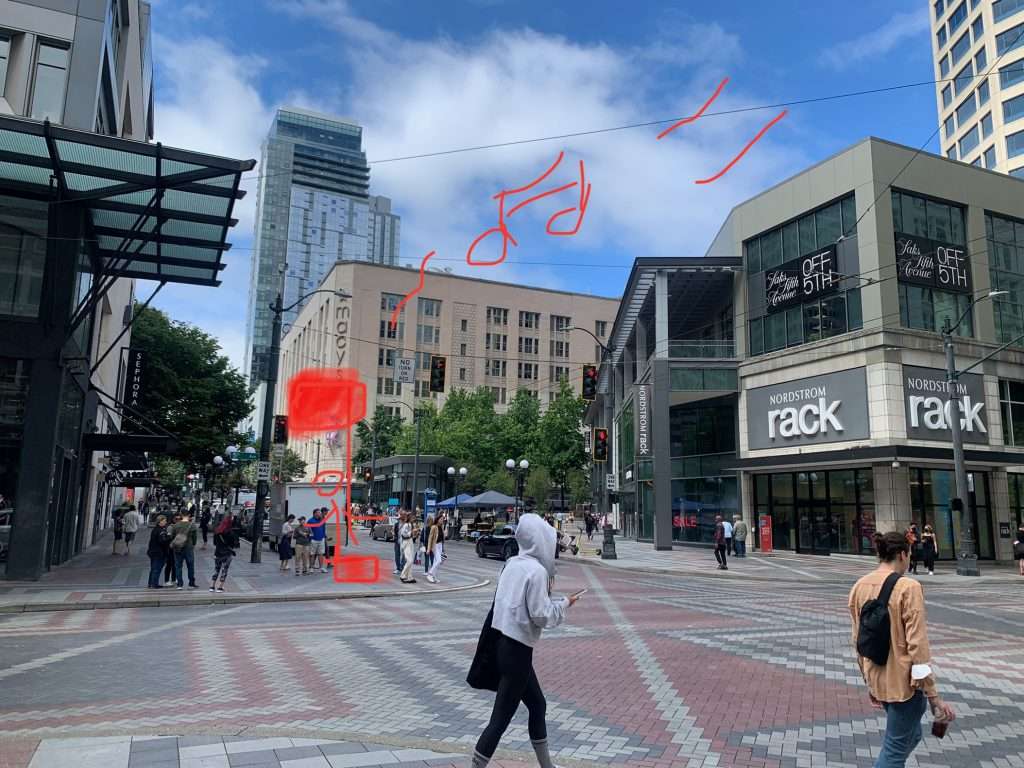 Busy intersection with pedestrians in downtown San Francisco. A stick image drawn in red shows a stick figure on a red box holding a red flag with musical notes floating in the sunny sky.